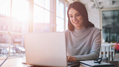 Applied Benefits A woman in a gray turtleneck, sitting at a desk while using her laptop